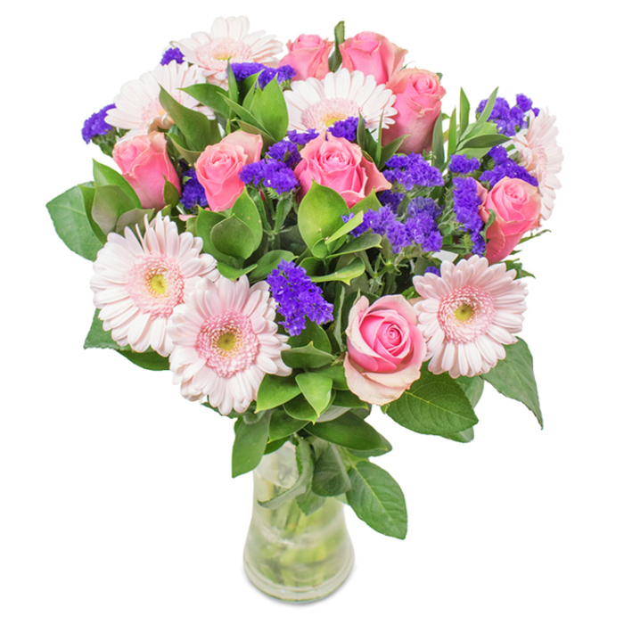 Presented against a crisp white background, this exquisite bouquet is a North Ockendon signature: a carefully balanced arrangement that seamlessly blends about eight medium pink roses-each one swirling open to reveal its iconic spiral-with a surround of five pale gerbera daisies. The gerberas' wide, pale pink petals are accentuated by creamy-white centers, their circular forms providing softness and unity. Vibrant purple statice is interwoven throughout, lending both textural intrigue and a subtle nod to the region's native wildflowers. Anchoring the display is a profusion of rich green foliage, its glossy leaves evoking the natural bounty found near Thames Chase Nature Reserve. All stems are artfully arranged in a clear glass vase, their lines visible through the sparkling water, underscoring the design's authenticity and freshness. Ideal as a thoughtful gift for occasions such as birthdays, anniversaries, or as a brightening addition to North Ockendon homes and offices, this bouquet exudes both joy and sophistication. Every botanical element is selected to convey sincere affection, warmth, and a sense of vibrant local artistry-a florist's tribute to the uplifting power of flowers delivered with care.